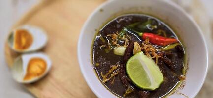 Rawon or Indonesian black beef soup, black color are from indonesian nut called kluwek. Served with lime, chili paste, salted egg, and tempe cracker. Perfect for recipe, article, or any cooking photo