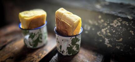 Ice chocolate drink on a vintage Indonesian iron mug with random green pattern called Blirik cup or cangkir Blirik on bokeh background along with chocolate filling bread photo