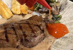 Sirloin steak grilled medium rare served with potatoes and salad with mushroom black pepper sauce in a restaurant photo