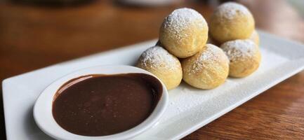 Homemade Dutch poffertjes mini pancakes with icing powdered sugar and chocolate fillings with additional chocolate sauce photo