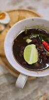 Rawon or Indonesian black beef soup, black color are from indonesian nut called kluwek. Served with lime, chili paste, salted egg, and tempe cracker. Perfect for recipe, article, or any cooking photo