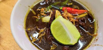 Rawon or Indonesian black beef soup, black color are from indonesian nut called kluwek. Served with lime, chili paste, salted egg, and tempe cracker. Perfect for recipe, article, or any cooking photo