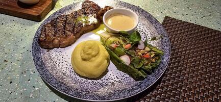 Beef New York strip loin steak or sirloin steak served with potatoes, and mushroom sauce and salad on plate photo