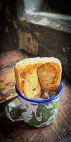 Ice chocolate drink on a vintage Indonesian iron mug with random green pattern called Blirik cup or cangkir Blirik on bokeh background along with chocolate filling bread photo