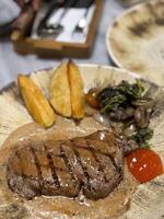 Sirloin steak grilled medium rare served with potatoes and salad with mushroom black pepper sauce in a restaurant photo