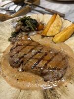 Sirloin steak grilled medium rare served with potatoes and salad with mushroom black pepper sauce in a restaurant photo