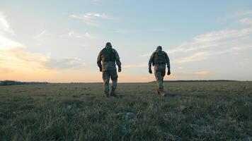 Soldaten Gehen durch öffnen Feld beim Dämmerung, zwei Soldaten im tarnen Ausrüstung Trekking über ein Feld. video