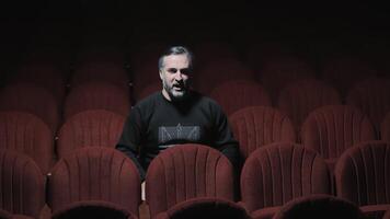 A singer sits alone in an empty opera house and sings. A lonely singer in a dark hall with red chairs. video