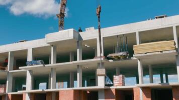 construcción de un casa. un construcción grua baja el carga. trabajo a el construcción sitio. monolítico de muchos pisos marco casa. video