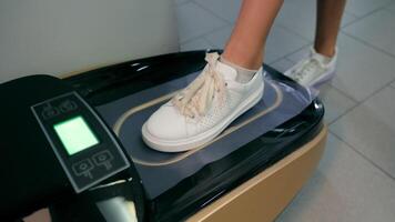 automatisch Schuh Abdeckungen im ein medizinisch Institution. ein Kinder Fuß im ein Weiß Sneaker steht auf das Maschine zum das automatisch Schaffung von Schuh Abdeckungen. video