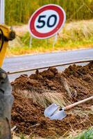 Arm of a mini digger and bucket with a speed limit sign at 50, road sign photo