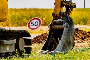 Arm of a mini digger and bucket with a speed limit sign at 50, road sign photo