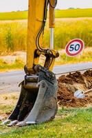 Arm of a mini digger and bucket with a speed limit sign at 50, road sign photo