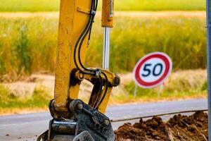 Arm of a mini digger and bucket with a speed limit sign at 50, road sign photo