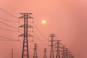 Electricity pillars against a colorful yellow sunset. Silhouette high voltage electric towers, power lines. photo