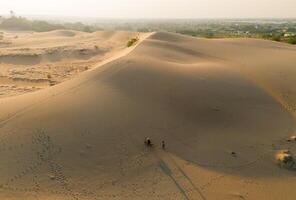 Aerial view of a peasant woman carries a bamboo frame on the shoulder across sand dunes in Ninh Thuan province, Vietnam. It is one of the most beautiful places in Vietnam photo