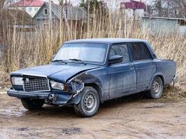 A neglected sedan with significant front-end damage sits abandoned on a dirt road, reflecting neglect and loss photo