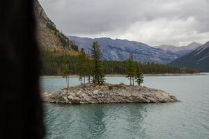 nublado día en rocoso isla en lago minnewanka, canadiense rocoso montañas, banff nacional parque foto