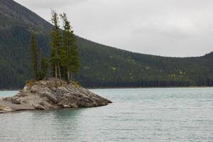 nublado día en rocoso isla en lago minnewanka, canadiense rocoso montañas, banff nacional parque foto