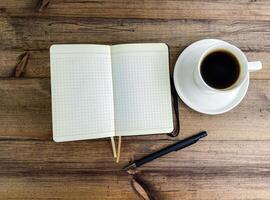 Coffee in a cup and a notebook with a pen on the table, top view. photo