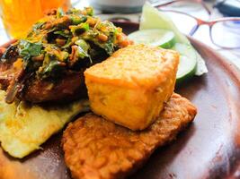 Indonesian Food. chicken penyet with chili sauce with tofu, tempeh, cucumber, egg and other fresh vegetables on wood plate photo