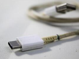 cerca arriba el blanco roto teléfono inteligente USB cable en blanco de madera antecedentes. foto