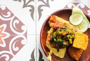 Indonesian Food. chicken penyet with chili sauce with tofu, tempeh, cucumber, egg and other fresh vegetables on wood plate photo