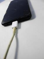 Old charger cable broken and smartphone, Defective charging cord, Connection deterioration device photo