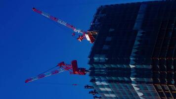 uma espaço de tempo do guindastes às a debaixo construção atrás a azul céu dentro Tóquio vertical video