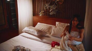 élégant femme dans une de mariée robe séance sur une lit dans une vaguement allumé, luxueux pièce avec une bouquet. video