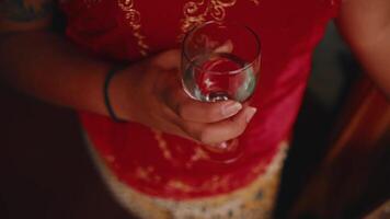 Close-up of a person in a red embroidered dress holding an empty wine glass, with a warm, intimate atmosphere. video