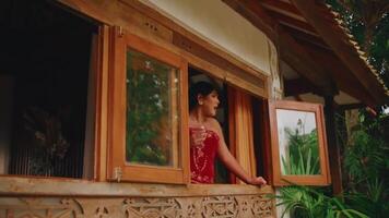 sereen vrouw staren uit van een rustiek venster omringd door weelderig groen. video
