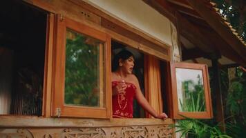 sereno donna guardando su a partire dal un' rustico di legno finestra, circondato di lussureggiante verde. video