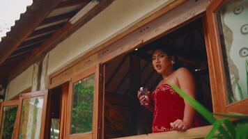 Elegant woman in red dress with wine glass by window video