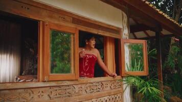 Person gazing out from a rustic wooden window frame, surrounded by lush greenery, evoking a sense of tranquility and connection with nature. video