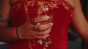 avvicinamento di un' donna nel un' rosso vestito Tenere un vuoto vino bicchiere, con un' messa a fuoco su il bicchiere e sua mano. video