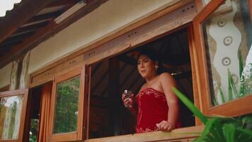 Woman in red dress looking out from a rustic cabin window. video