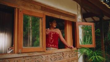 Person enjoying a tropical view from a rustic window in a wooden cabin surrounded by lush greenery. video