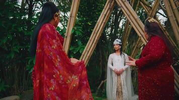 twee Dames in traditioneel rood kleding dansen Bij een cultureel evenement met bamboe structuren video