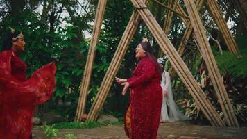 twee Dames in traditioneel rood kleding dansen Bij een cultureel evenement met bamboe structuren video