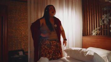 Woman standing by a bed in a dimly lit room, expressing surprise or shock. video