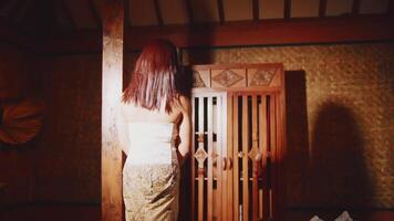 Rear view of a woman with red hair wearing traditional clothing, standing in a room with wooden walls video