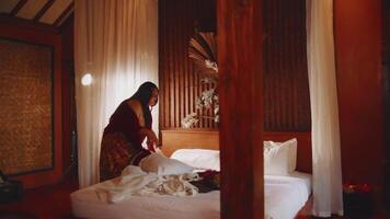 governante preparazione un' letto nel un' accogliente, calorosamente illuminato Hotel camera con elegante arredamento. video