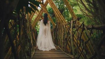 novia en pie en un de madera puente en un bosque, enmarcado por un arco de sucursales. video