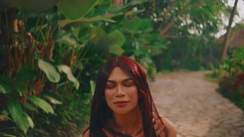 sereno mujer con rojo pelo disfrutando un tranquilo jardín camino rodeado por lozano verdor. video