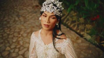 Elegant bride in a vintage dress and tiara posing outdoors on a cobblestone path. video