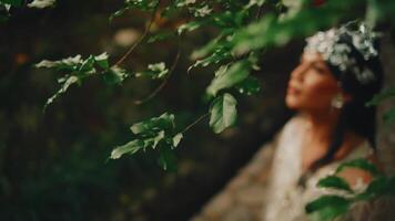 novia en cordón vestir con floral fuente en pie debajo árbol sucursales, suave enfocar, romántico atmósfera. video