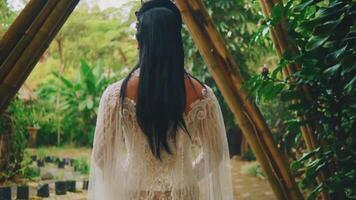 Rear view of a woman in a bohemian dress standing in a lush garden, surrounded by greenery video