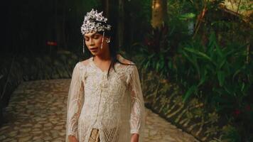 elegant kvinna i en årgång klänning och blommig huvudstycke stående i en lugn skog miljö. video