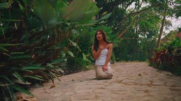 elegante mujer posando en un tropical jardín camino rodeado por lozano verdor y exótico plantas video